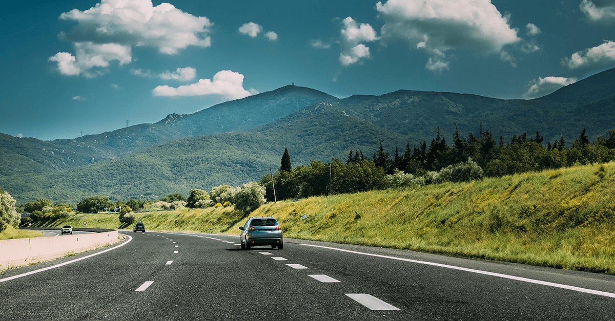 Auto fährt auf Landstrasse vor Bergkulisse – Symbol für Mobilität und Unabhängigkeit durch Finanzierung mit einem Autokredit